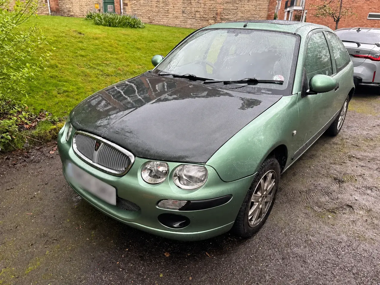Carbon fibre bonnet fitted to a green Rover 25, with the registration plate blurred